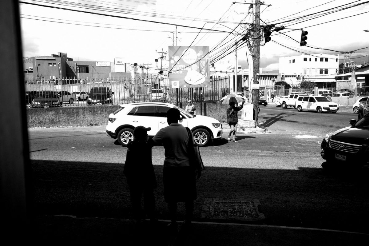 This guy holds one hand up while the other holds and umbrella while crossing the road at a dangerous spot.  The woman in the foreground holds the boy as they attempt the same river crossing of death.